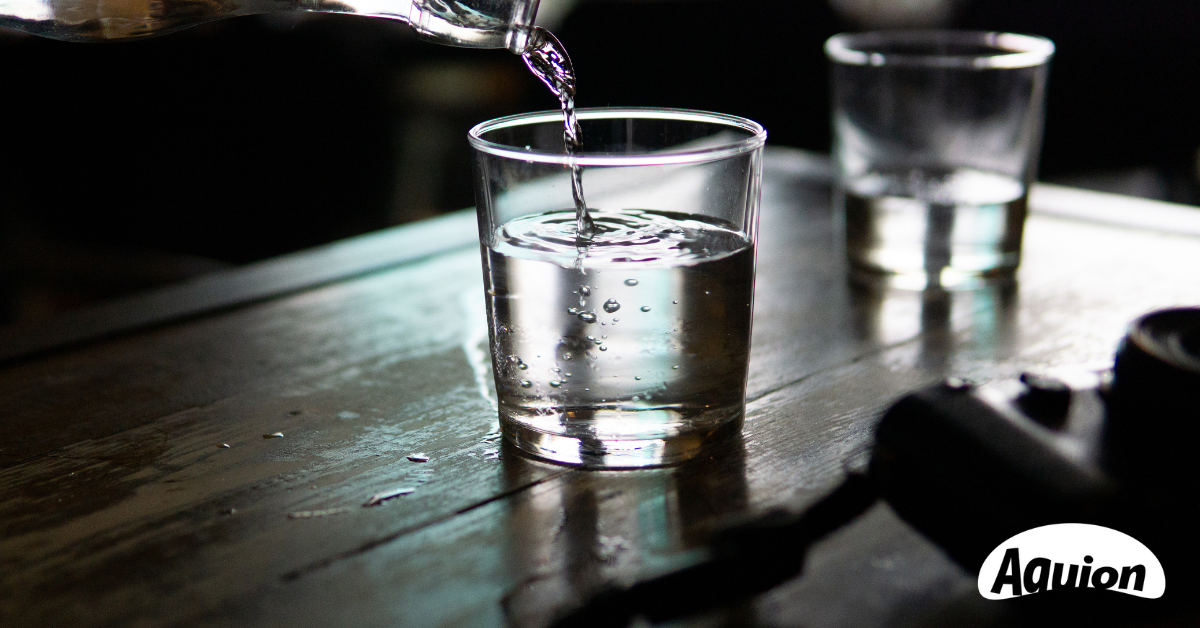 Glasflasche mit Wasser füllt ein Glas - AQUION ist Teil des Refill-Netzwerks