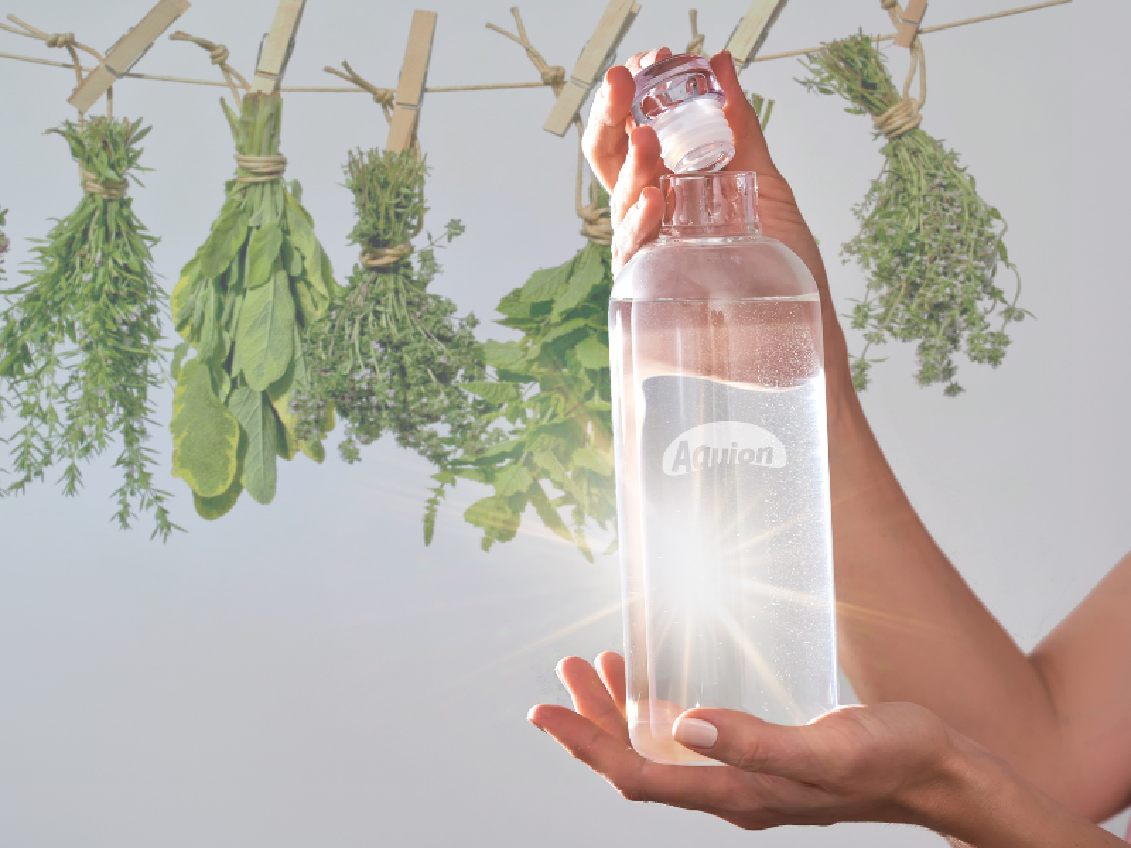 Eine Flasche Wasser wird in der Hand gehalten. Hinten im Bild sind getrocknete Kräuter in Büschel zu sehen, die zu den Bitterstoffen gehören.